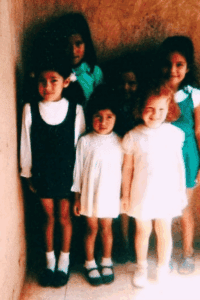 Four children standing together indoors, smiling at the camera.