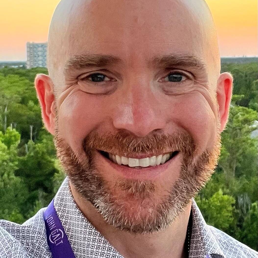 Smiling man with a beard outdoors at sunset.