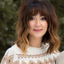 Woman with brown hair and bangs smiling outdoors.